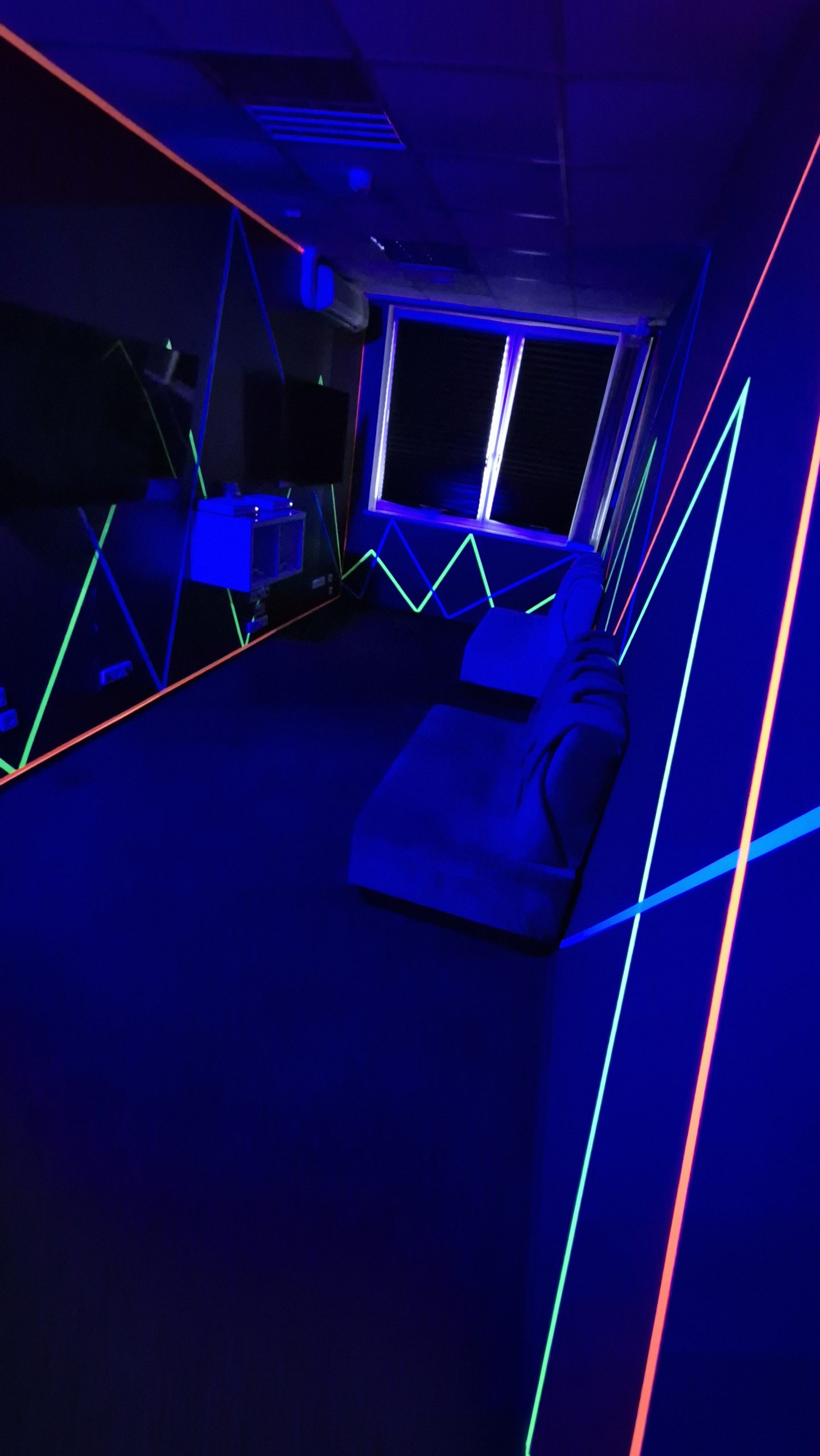 VRspotas gaming kambarys su sofomis, ekranais ir neoninėmis sienomis