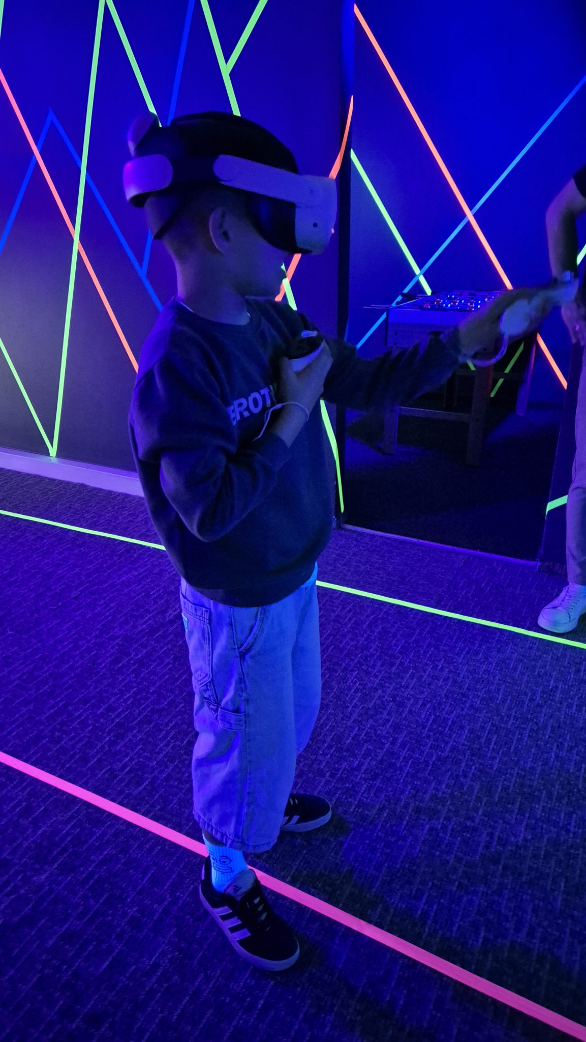 VR žaidėjas UV šviesoje švytinčių neoninių arenos sienų fone